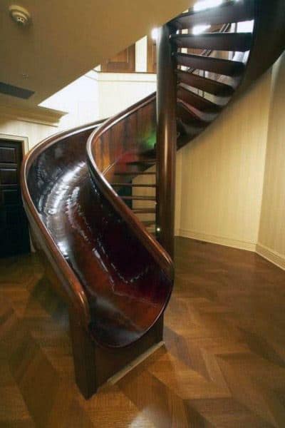A polished wooden slide spirals gracefully alongside a staircase on shiny parquet flooring