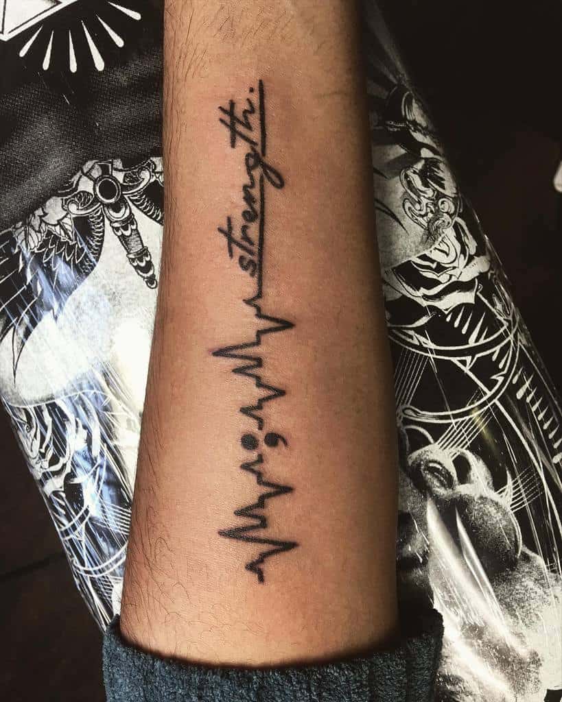 The tattoo features a semicolon integrated with an EKG heartbeat line and the word "strength" written in a delicate script.