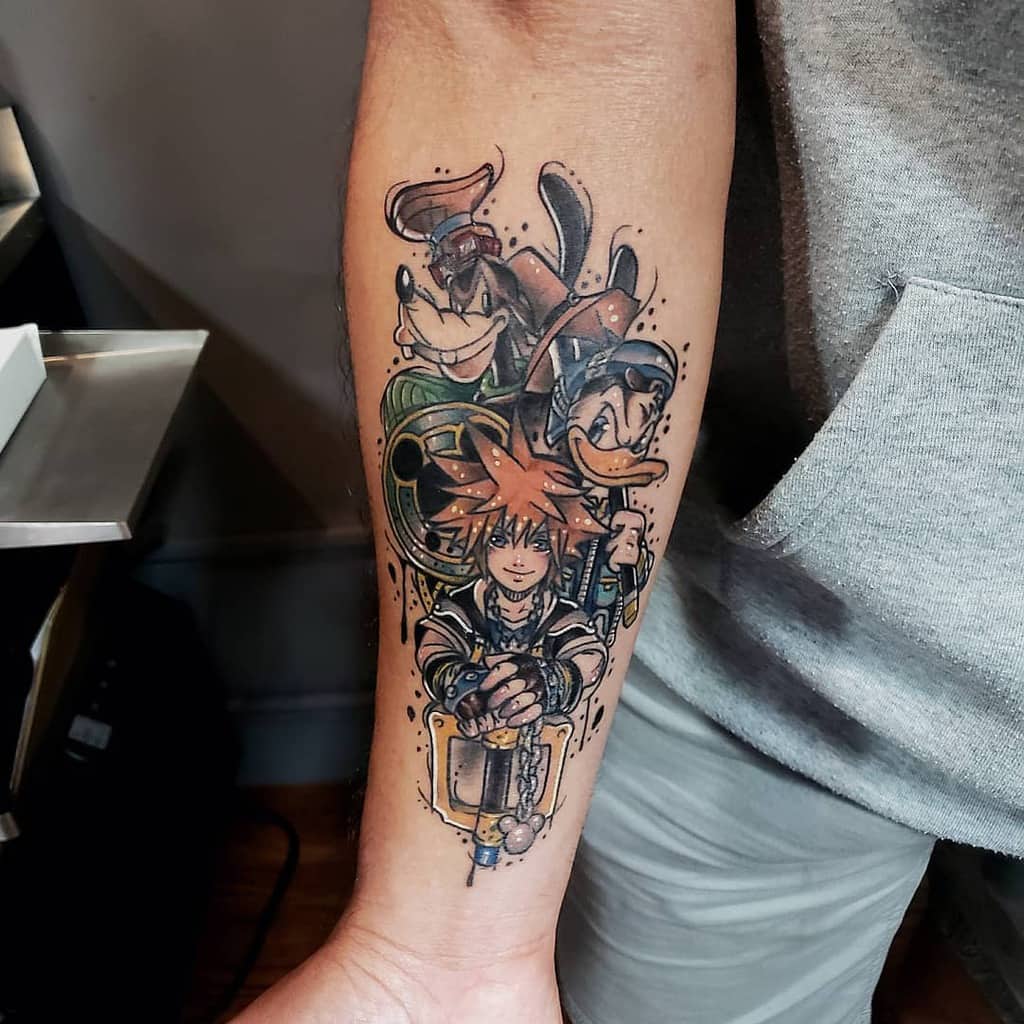 Vibrant Kingdom Hearts tattoo featuring Sora, Donald, and Goofy with a Keyblade, detailed shading, and dynamic colors on the forearm.
