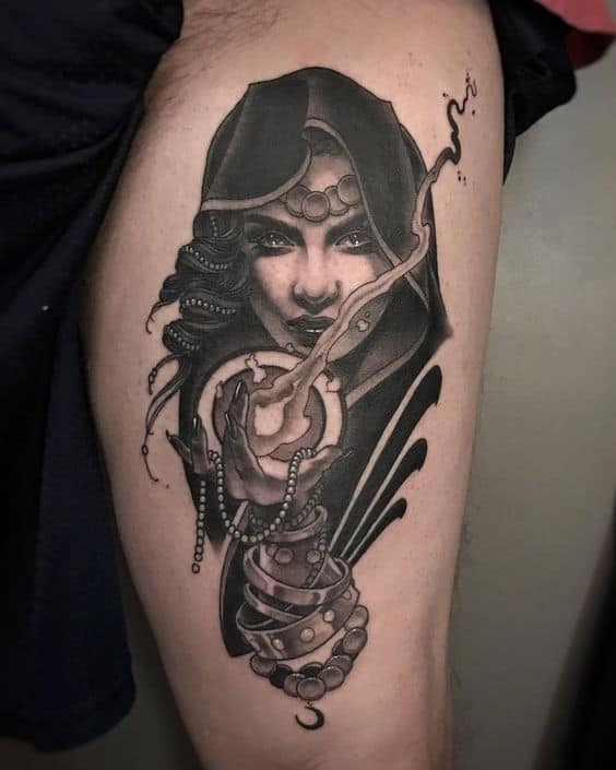 Dark and mystical black and grey tattoo of a hooded sorceress conjuring magic from a glowing orb, with intricate shading on the thigh.