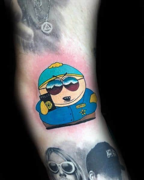 South Park tattoo of Cartman as a cop, wearing sunglasses and holding a police badge, with bold colors and a red background accent.