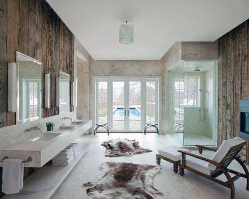 Rustic bathroom with wooden walls, glass shower, animal print rugs, and large window view