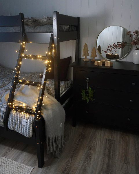 Cozy black bunk bed with warm string lights on the ladder, paired with a minimalist dresser and rustic holiday decor