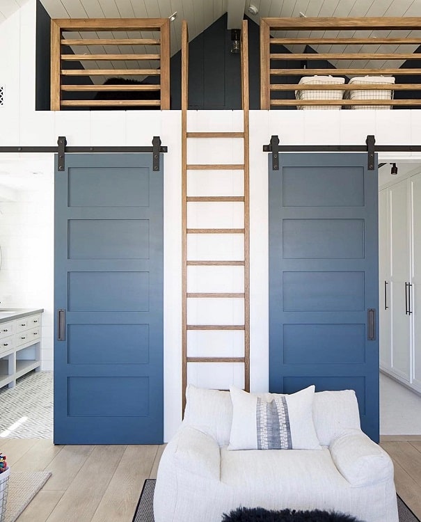 Blue single sliding barn doors with a wooden loft ladder in a modern white living space.