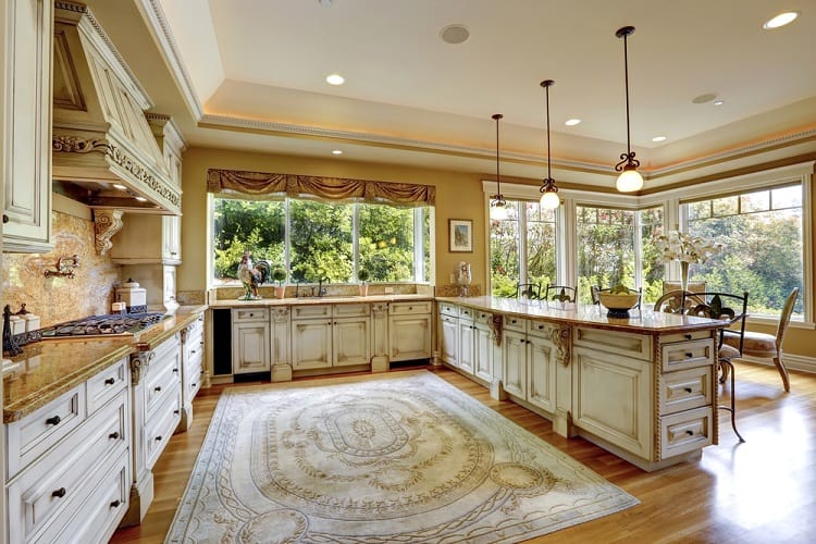 A spacious kitchen featuring a tray ceiling, elegant cabinetry, large windows with a beautiful view, and a decorative rug, creating a warm and inviting atmosphere
