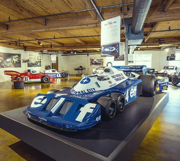 A spacious garage featuring race cars under a rustic wood-beam ceiling.