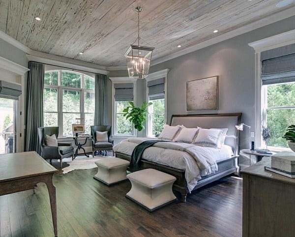 Rustic bedroom with wood ceiling large windows candelabra chandelier and seating area.
