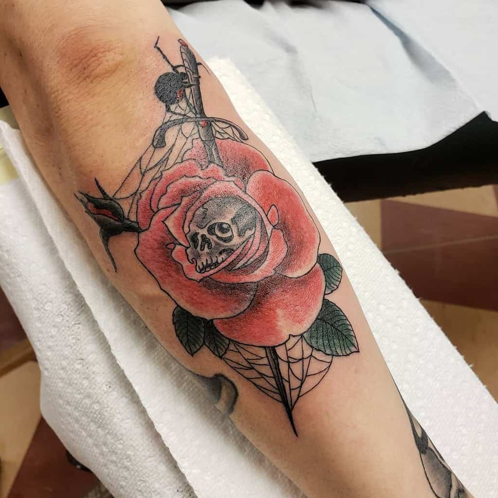 Neo-traditional tattoo of a red rose with a hidden skull inside, wrapped in spiderwebs and branches, creating a dark yet elegant design.
