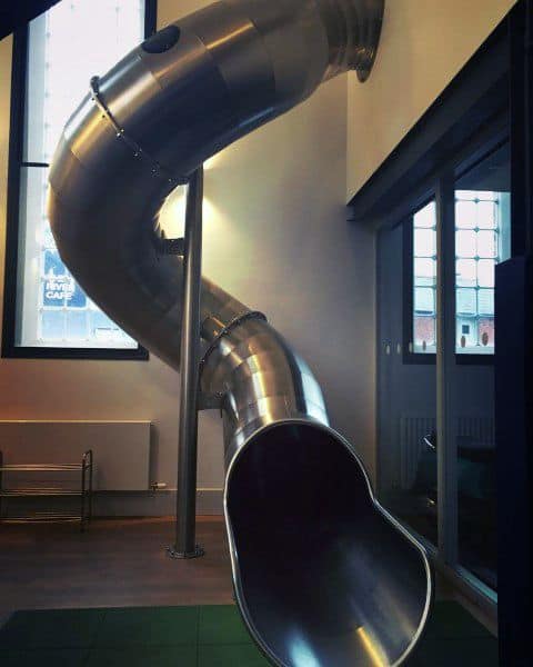 A massive indoor slide spirals down from the ceiling in a modern room
