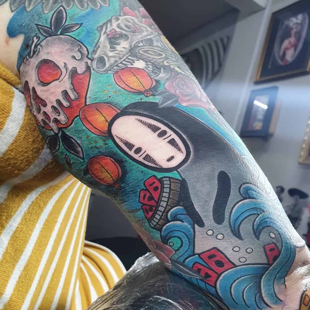 Vibrant Spirited Away tattoo sleeve featuring No-Face floating on waves, surrounded by lanterns, buildings, skull in apple, dinosaur skull