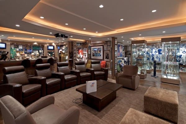 A cozy home theater room with leather recliners, sports memorabilia on display, and a well-lit ceiling