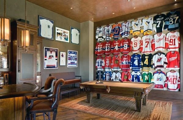 Man cave with numerous hockey jerseys on the wall and a wooden pool table at its center