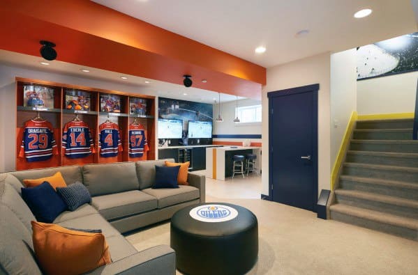 Basement sports room with jerseys on display, a couch, and a TV wall near a staircase