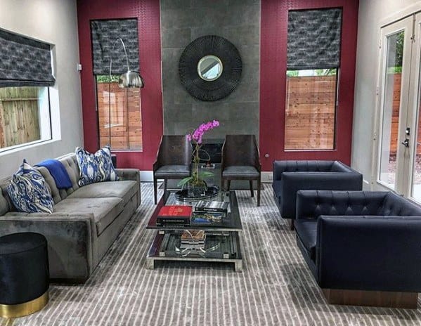 Grey daybed couch with blue accent pillows in a modern living room featuring black armchairs and a glass coffee table.