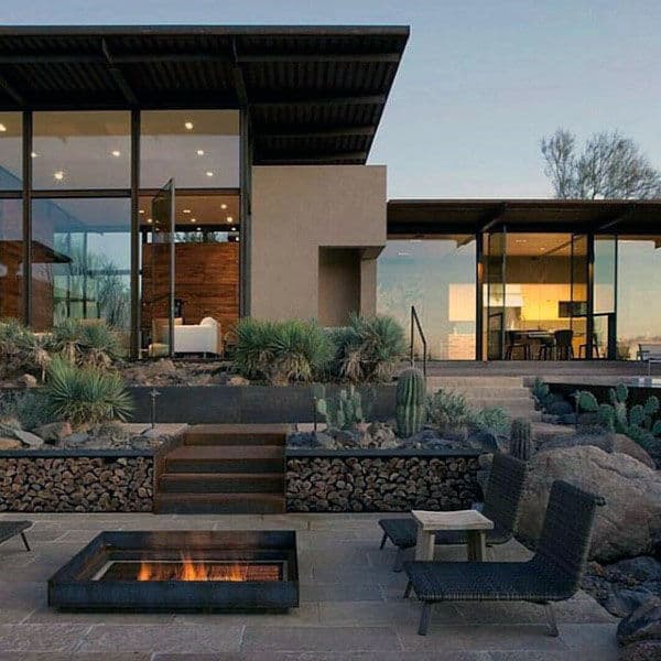 A modern house with large glass windows and a landscaped patio featuring a fire pit and seating area