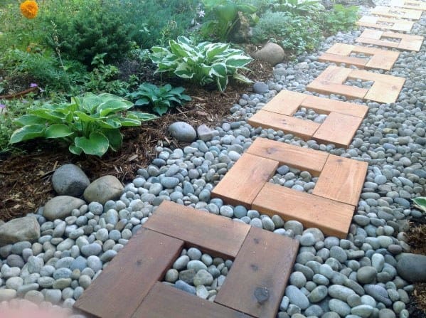 A garden walkway with square stone tiles surrounded by pebbles and plants
