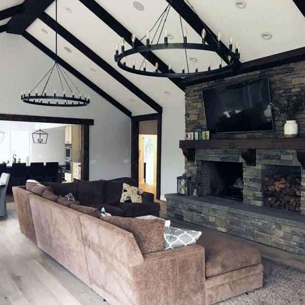 Cozy living room with stacked stone fireplace, brown sofa, and large chandeliers