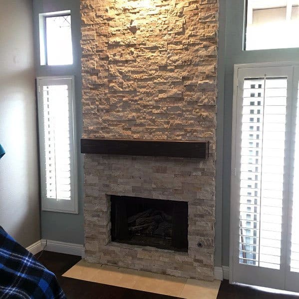 Stacked stone fireplace with tall windows and white shutters in a brightly lit room
