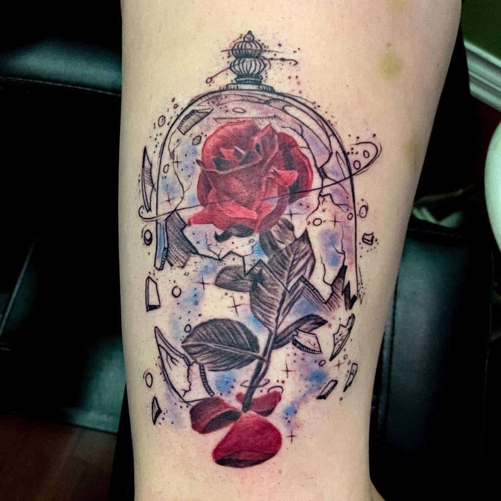A vibrant tattoo of the iconic Beauty and the Beast rose in a shattered glass dome with watercolor accents