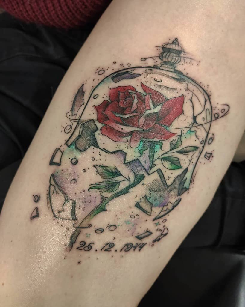 A colorful Beauty and the Beast-inspired tattoo featuring a rose in a shattered glass dome with a meaningful date beneath it