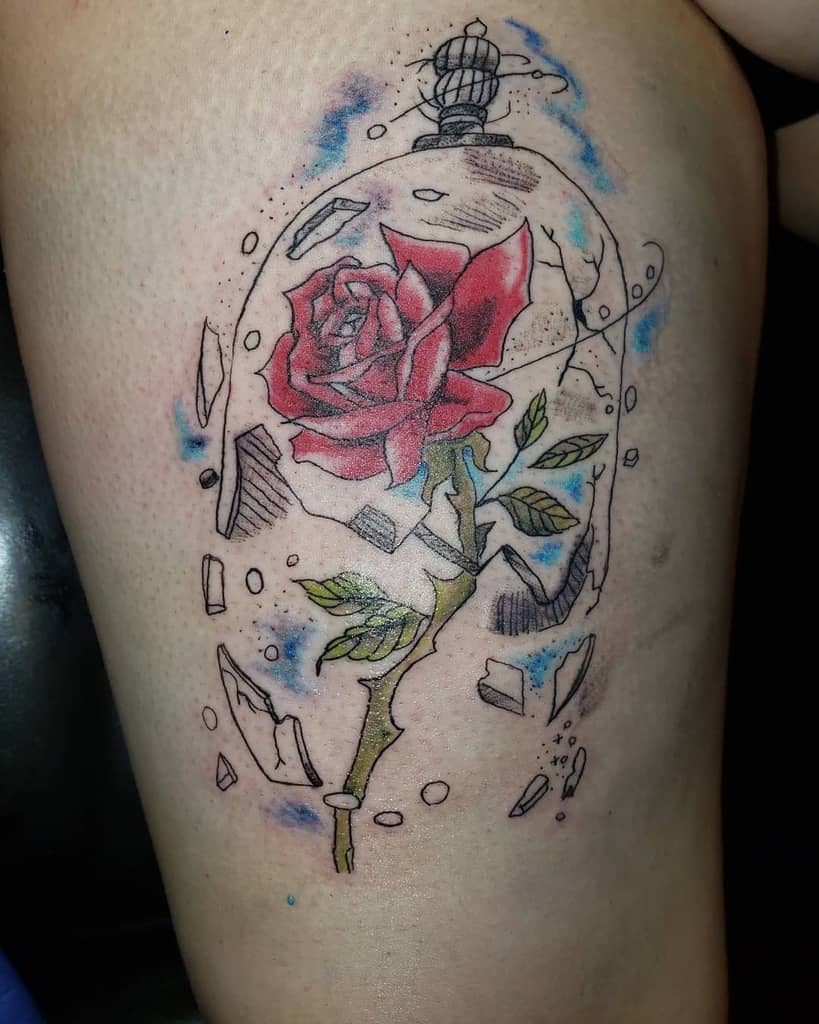 A tattoo of a red rose inside a broken glass dome, with shards of glass scattered around and soft blue accents