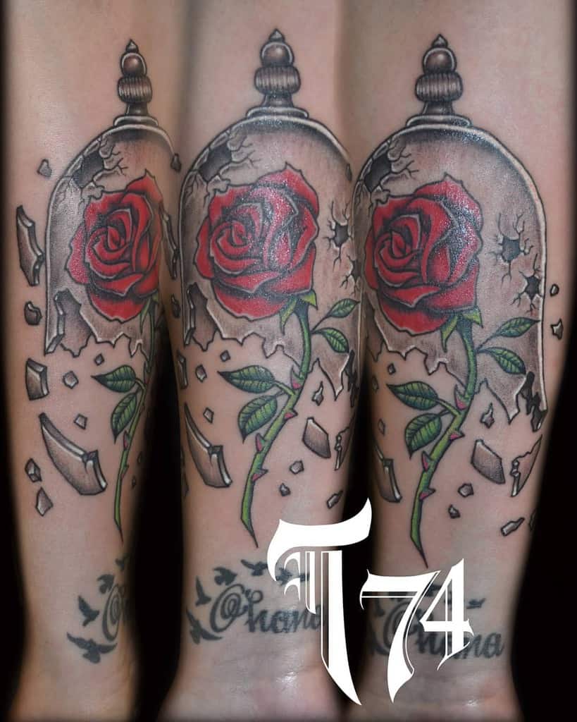 A tattoo featuring multiple Beauty and the Beast roses inside glass domes, surrounded by shattered glass with vibrant red and green details