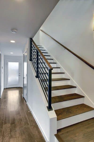 Wooden staircase with horizontal metal handrails in a modern hallway with hardwood floors.