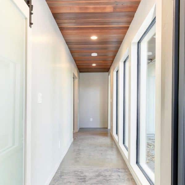 Modern hallway with stained wood ceiling, large windows, and white walls.