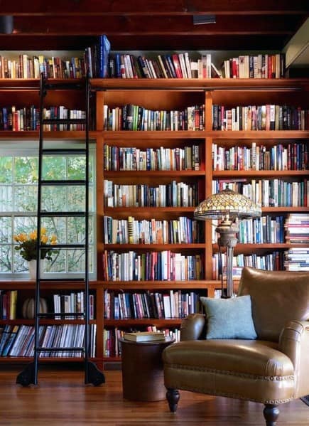 A cozy library with a leather chair, lamp, and a tall bookshelf ladder