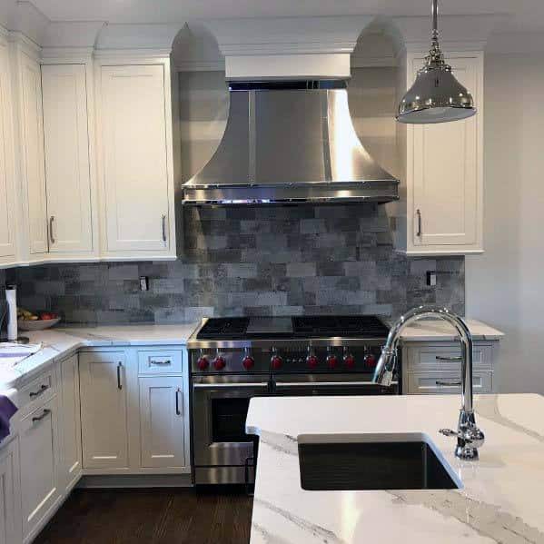 stainless steel range hood in white cabinet kitchen with gray tile backsplash