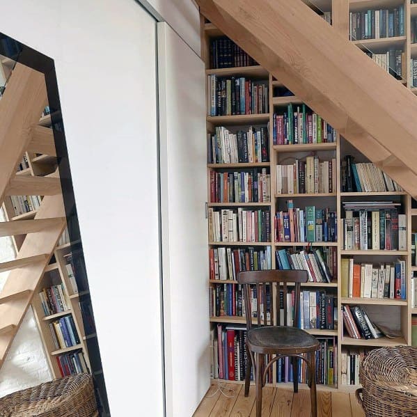 Cozy library corner with wooden bookshelves, a chair, and a slanted wooden ceiling