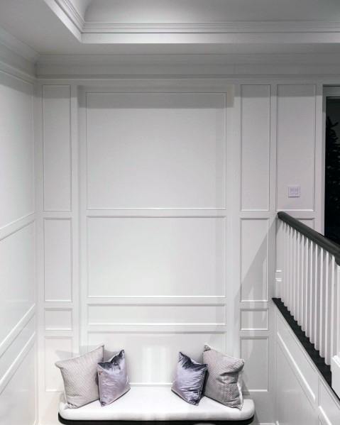 Elegant staircase hallway with luxury crown molding, white paneled walls, and a simple bench with decorative pillows