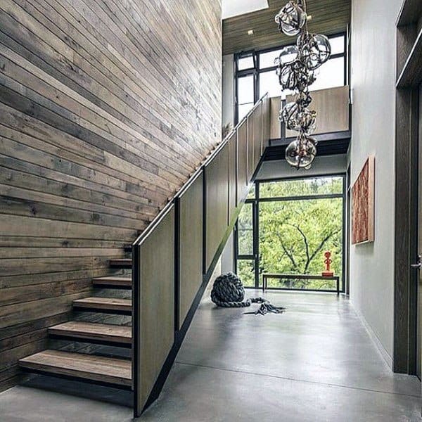 A modern staircase with wooden panels and an abstract chandelier in a sunlit room, leading to panoramic window views