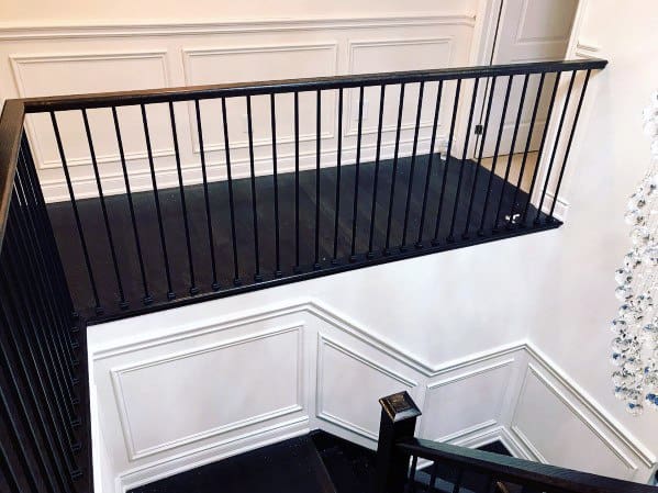 Black railing on a staircase landing with white paneled walls and chair rail in the background