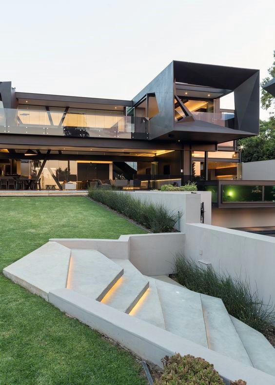Modern home with geometric architecture, illuminated concrete steps, and a manicured lawn.