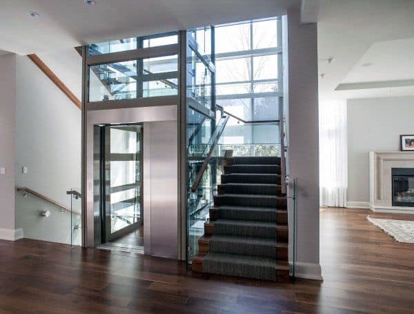 Modern home interior with a glass elevator, wooden flooring, a striking staircase, and a large window