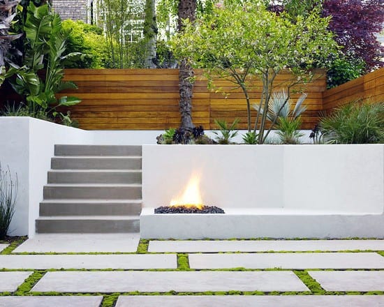 Modern backyard with concrete steps, built-in fire pit, white walls, and wooden privacy fencing.
