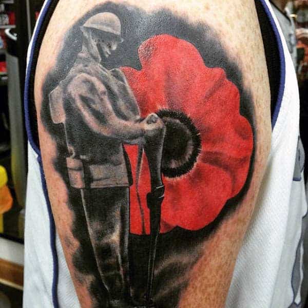 Tattoo of a soldier in grayscale with a large red poppy in the background on an upper arm