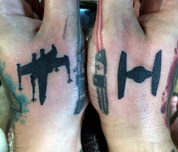 Two hands with tattoos of an X-Wing on one hand and a TIE Fighter on the other hand