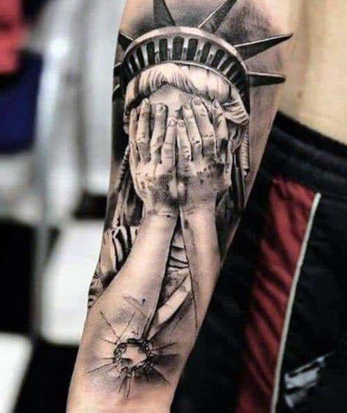 Tattoo of the Statue of Liberty covering her face, paired with a shattered bullet hole, symbolizing sorrow, disillusionment, or protest.