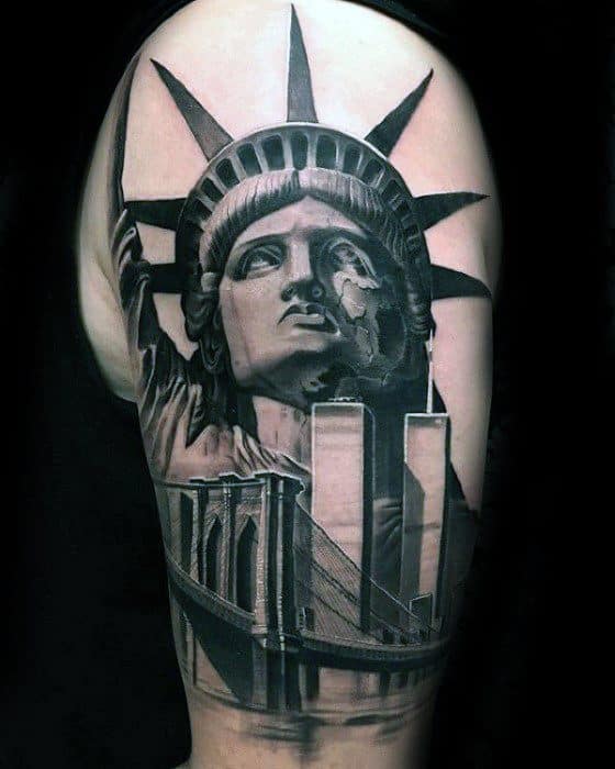 Realistic upper arm tattoo of the Statue of Liberty with Brooklyn Bridge and Twin Towers, done in bold black and gray shading.