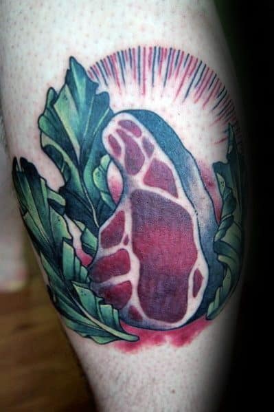 Tattoo of a raw steak surrounded by leafy greens, with a radiant glow effect, creating a bold and vibrant food-inspired design.