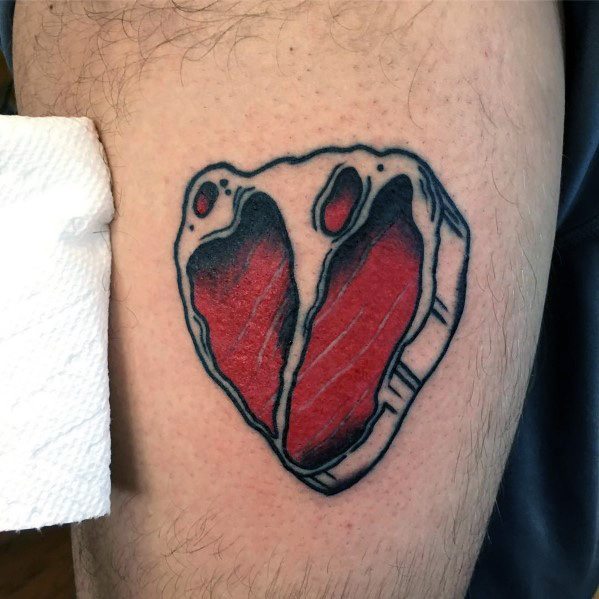 Tattoo of a heart-shaped steak with bold black outlines and red shading, creating a striking and unique meat-inspired design.