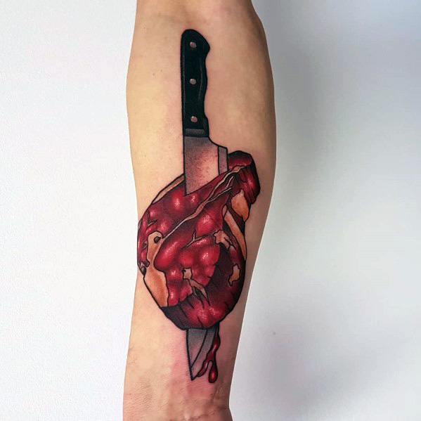 Tattoo of a realistic anatomical heart made of raw meat, pierced by a large knife, with bold shading and dripping details for a striking design.