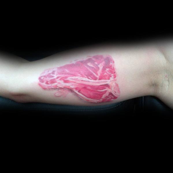 Tattoo of a realistic raw steak with detailed marbling and shading, placed on the inner arm for a bold and lifelike meat-inspired design.