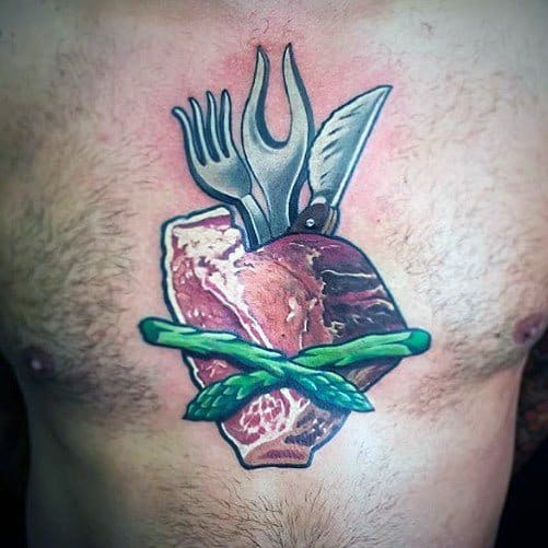 Tattoo of a raw steak shaped like an anatomical heart, pierced by a knife and fork, wrapped in asparagus, creating a bold and unique design.