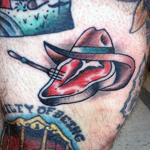Tattoo of a steak wearing a cowboy hat, pierced by a fork, blending Western and food themes with bold outlines and shading for a fun design.