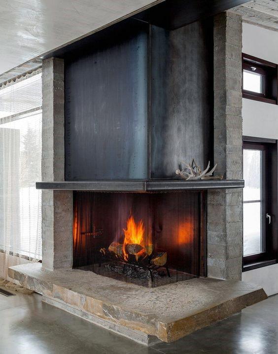 Industrial-style corner fireplace with a black steel hood, stone base, and exposed brick sides.