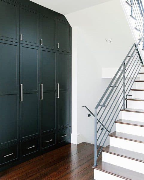Staircase with sleek railing beside dark cabinets on wooden floor