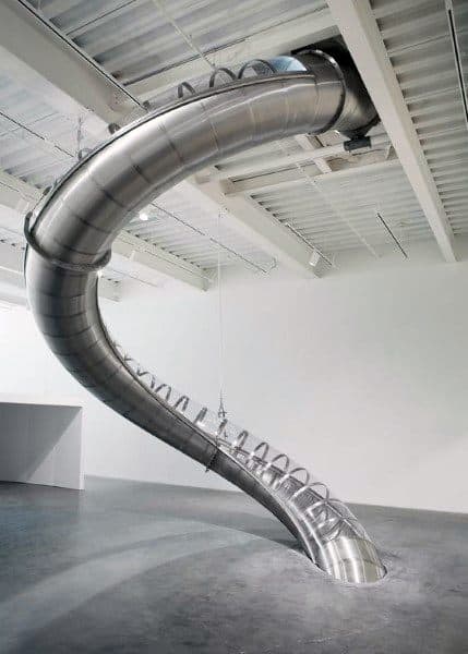 A large, twisting slide descends from the ceiling in a spacious, industrial-style room
